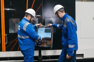 Two engineers operating CNC machinery in a factory setting, wearing safety gear and uniforms.
