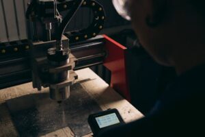 A detailed view of a CNC machine being operated by a person indoors with dim lighting.